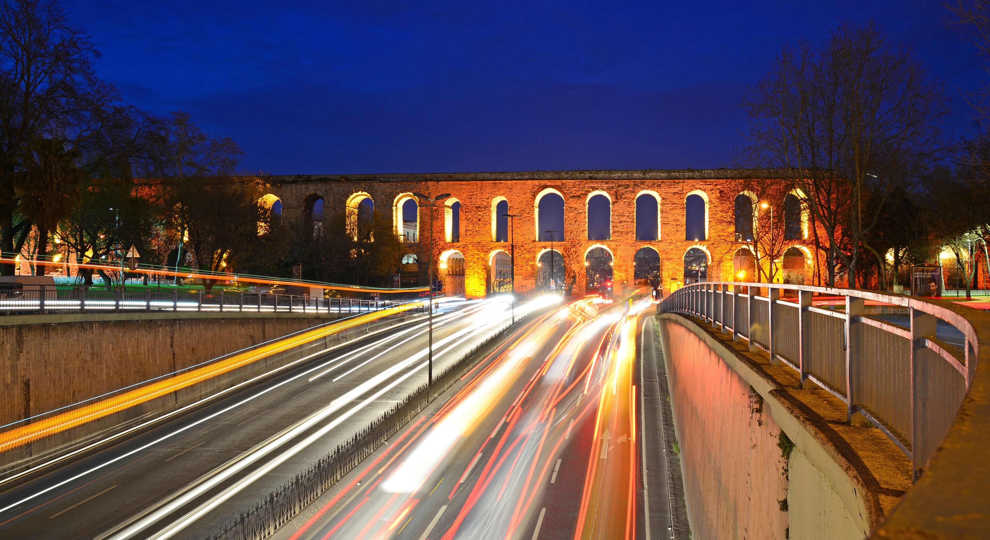 A long-exposure night scene of a bridge with illuminated arches and a road with light trails.