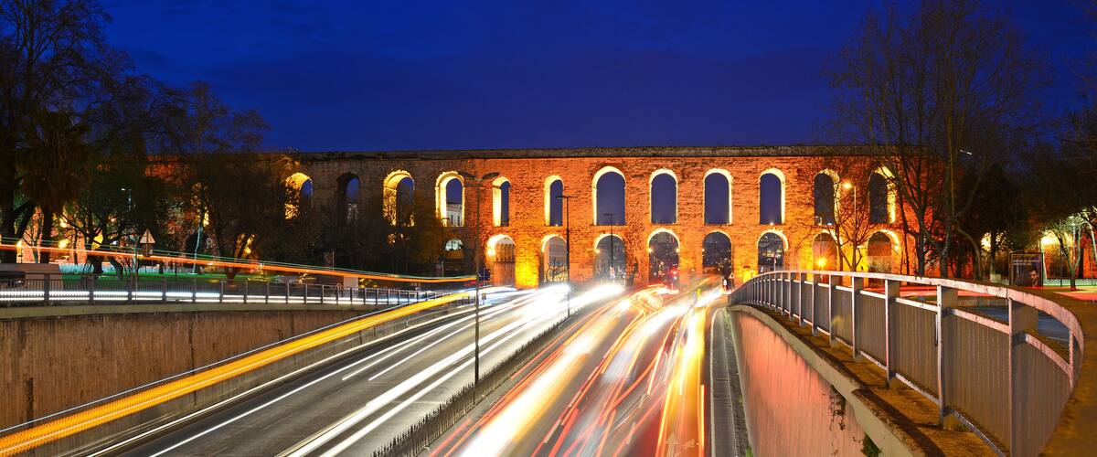A long-exposure night scene of a bridge with illuminated arches and a road with light trails.