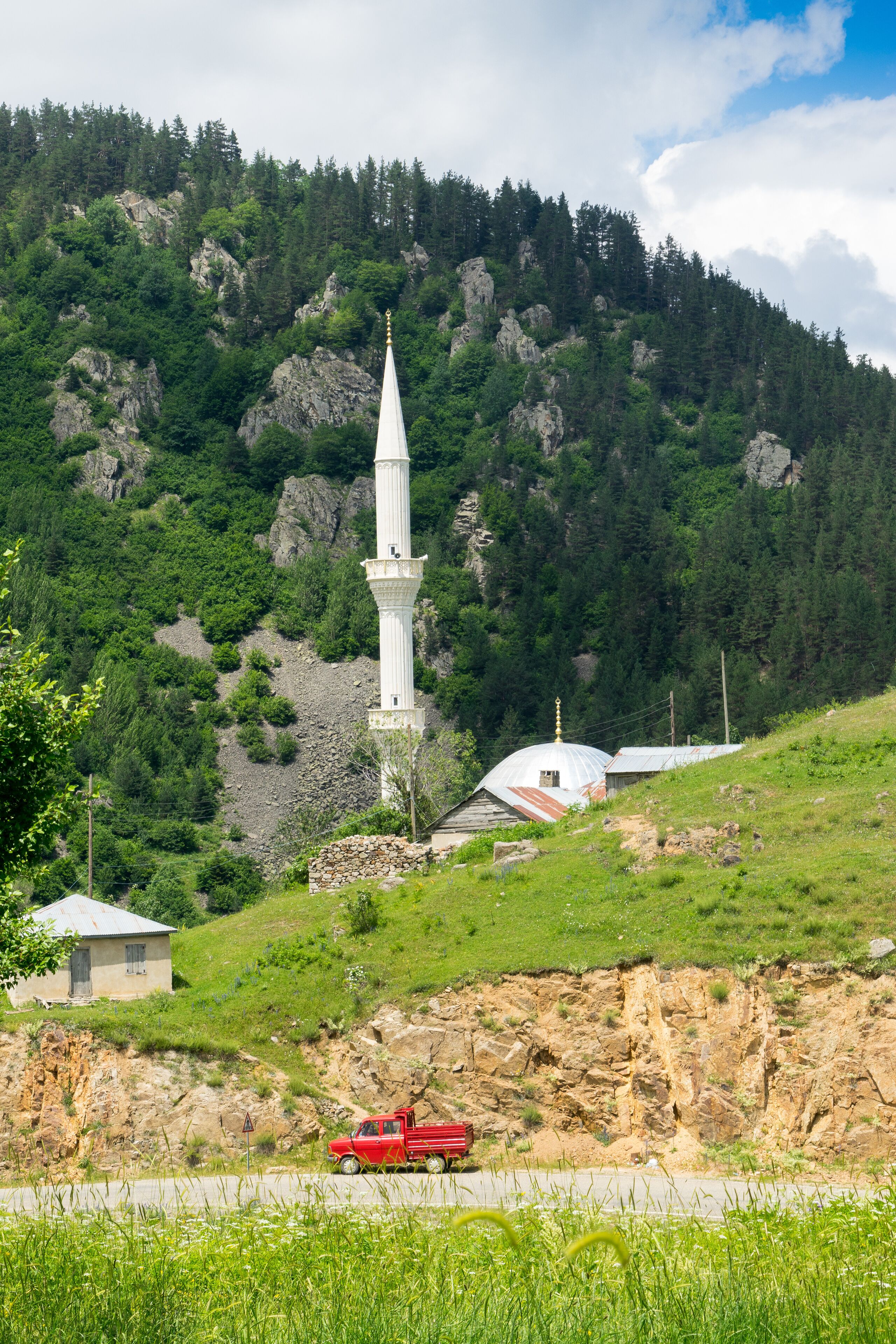 A white church with a tall spire, a red truck on a road, and a mountainous backdrop.