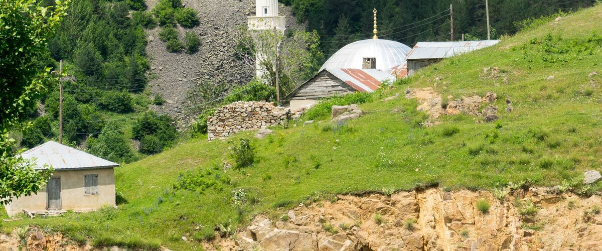 A white church with a tall spire, a red truck on a road, and a mountainous backdrop.