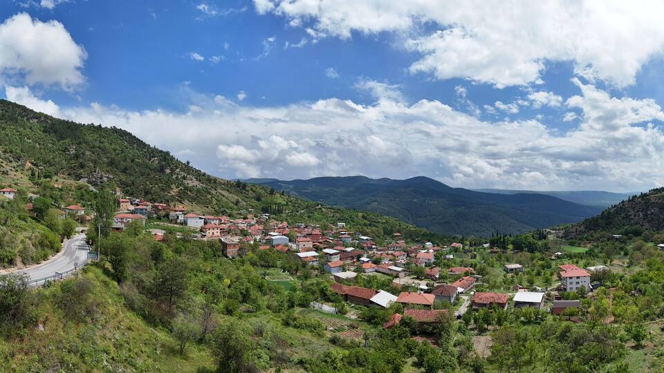 Stunning panoramic aerial view of Kemaliye village in Keles, Bursa, Turkey. Surrounded by lush green hills, traditional houses, and a winding mountain road under dramatic cloudy sky Turkiye panorama