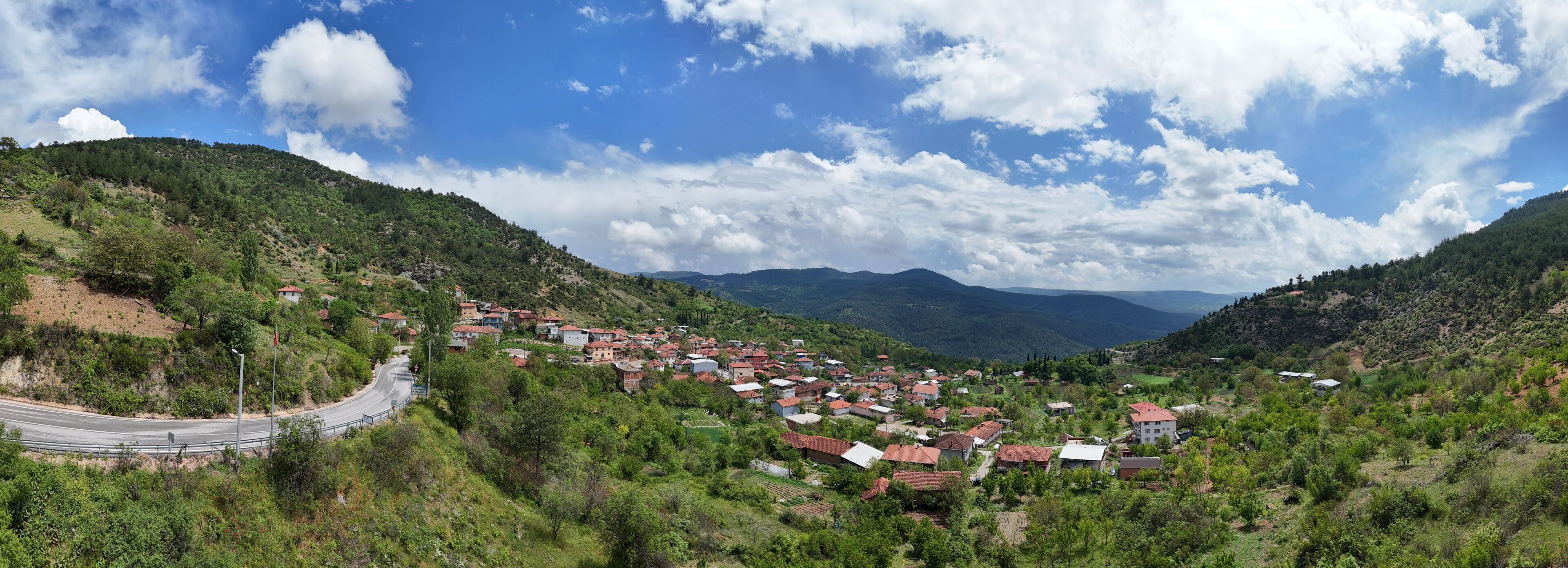 A village nestled in a valley surrounded by hills, with a winding road leading into the distance.