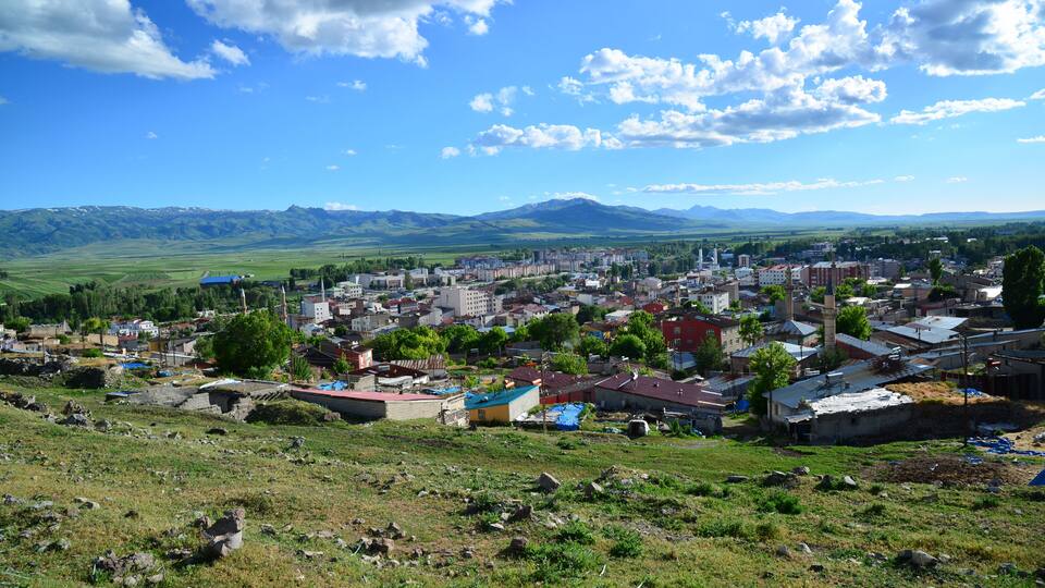 A town with a mix of modern and traditional buildings, surrounded by green fields and mountains in the distance.