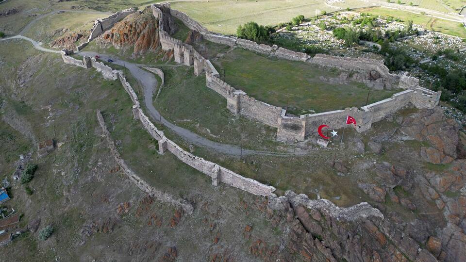 An ancient fortress with a surrounding wall and a small flag.