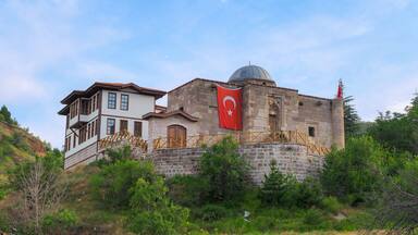 A historical building with a dome and a flag, surrounded by greenery and hills.