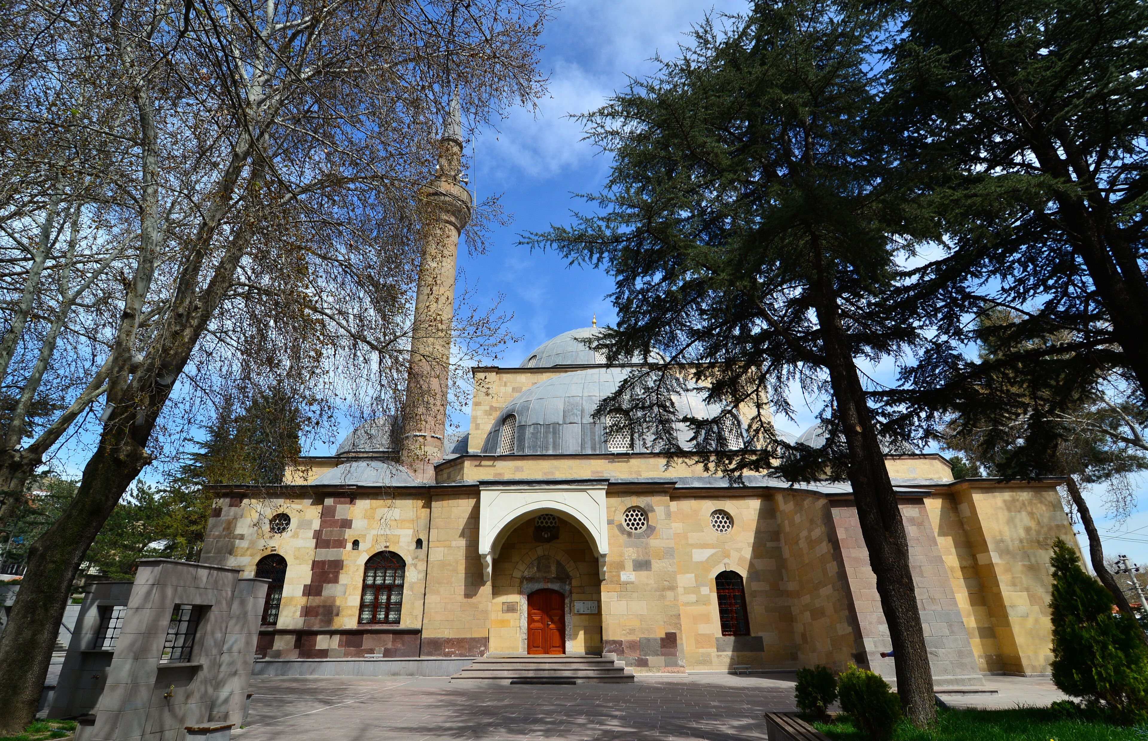 A historic building with a prominent minaret and a dome, surrounded by trees.