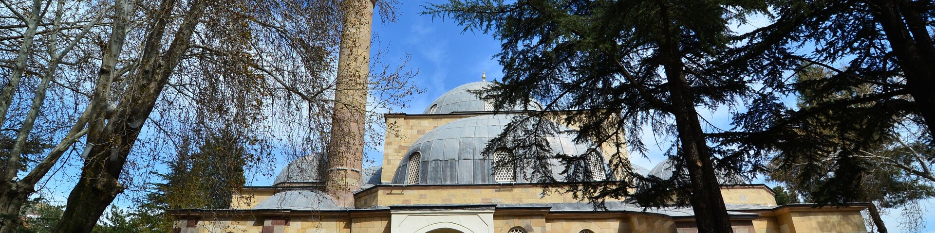 A historic building with a prominent minaret and a dome, surrounded by trees.