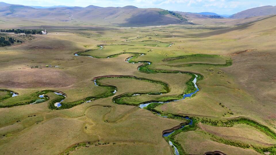 A river winding through a valley with rolling hills and sparse vegetation.