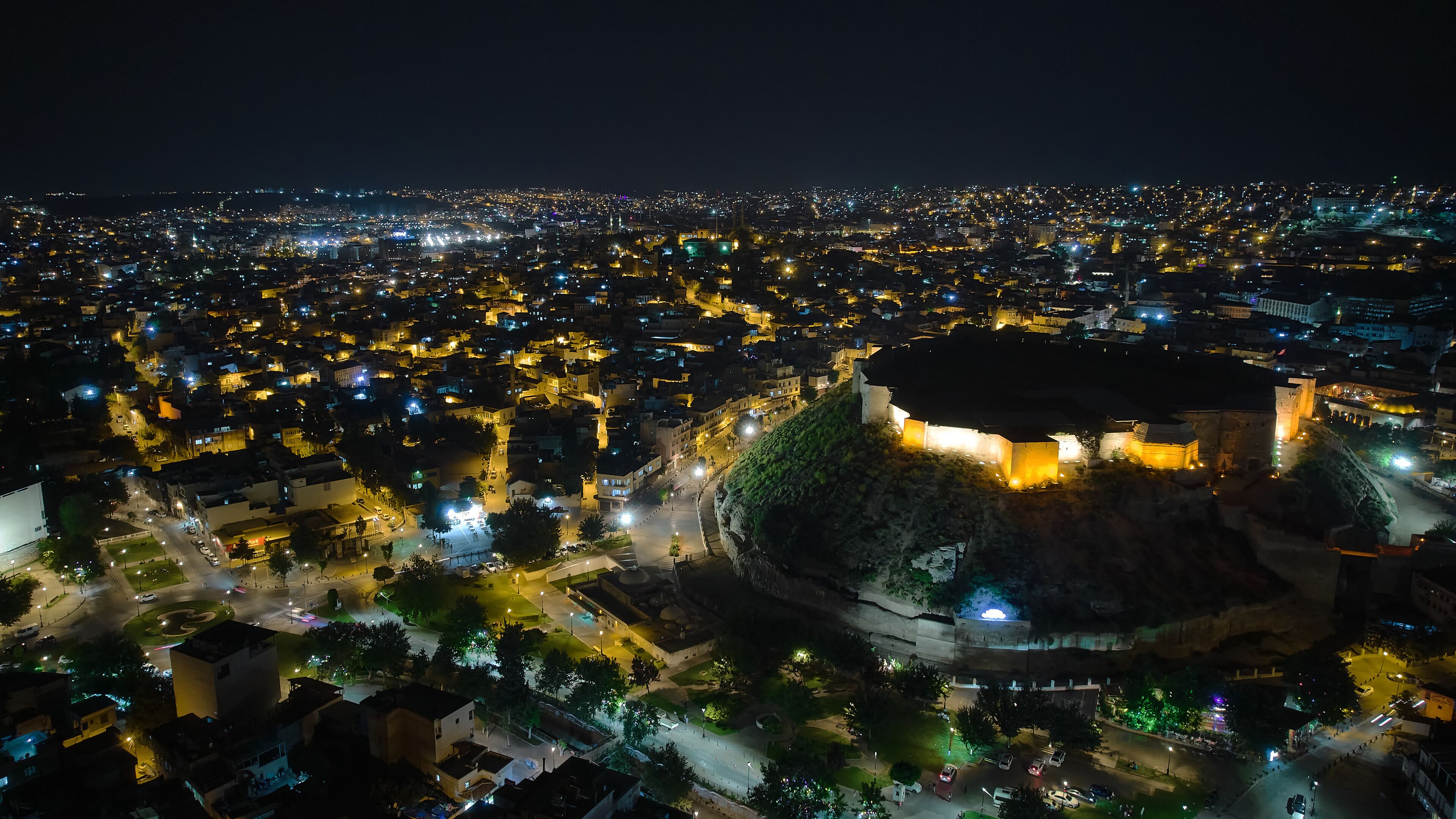A cityscape at night with a prominent castle-like structure surrounded by illuminated streets and buildings.