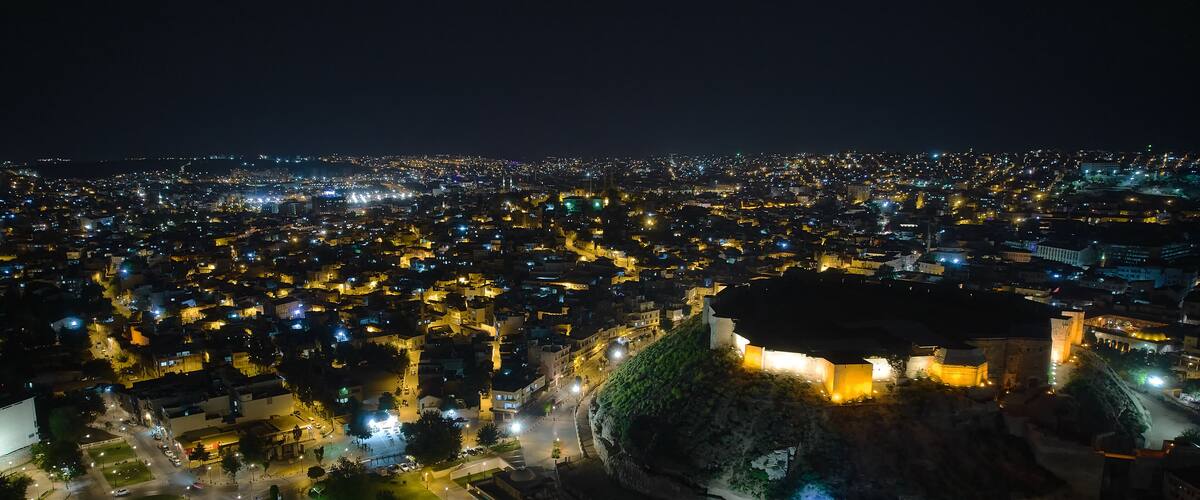 A cityscape at night with a prominent castle-like structure surrounded by illuminated streets and buildings.