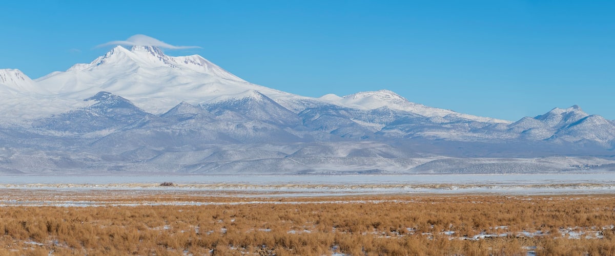 A snow-covered mountain range with a flat, grassy plain in the foreground.