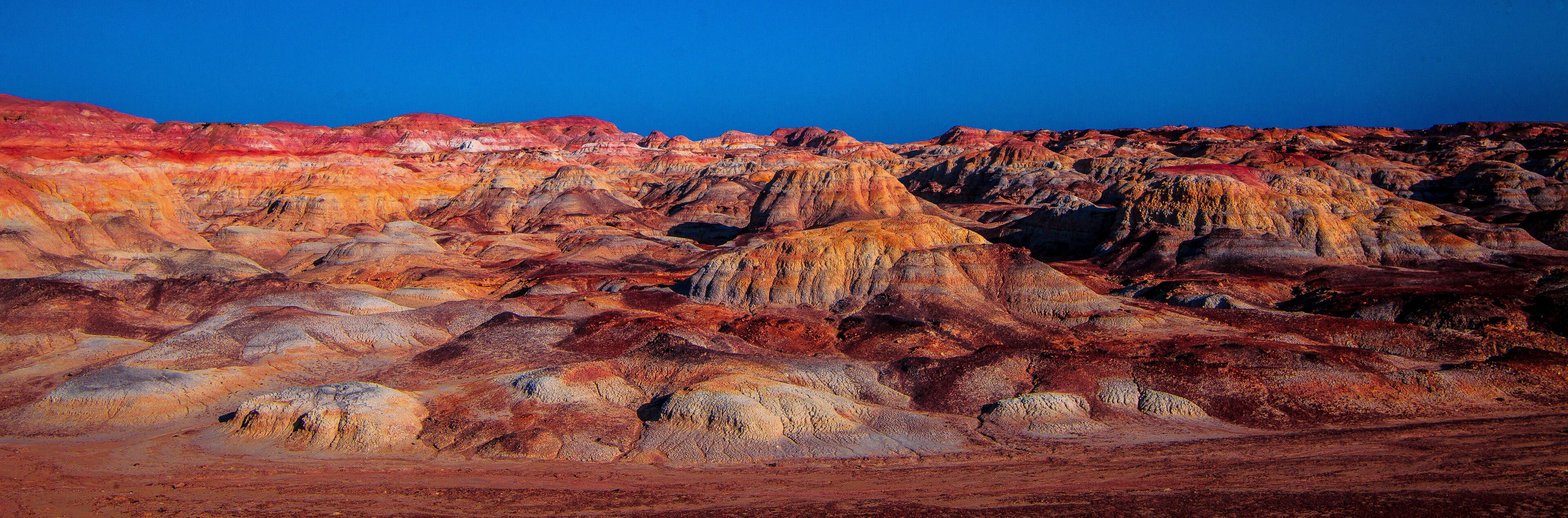 A rugged, colorful landscape with layered rock formations and a clear blue sky.