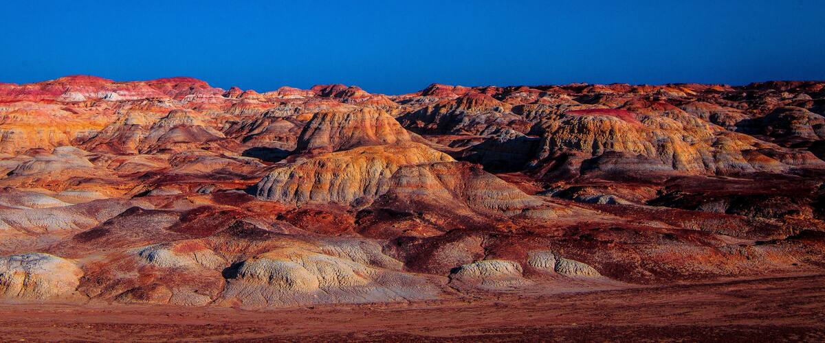A rugged, colorful landscape with layered rock formations and a clear blue sky.