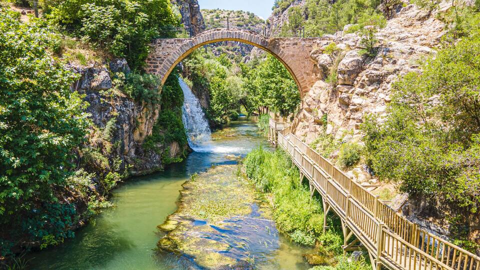 A stone bridge over a river, surrounded by greenery and rocky cliffs.