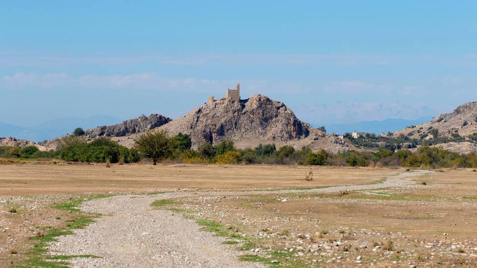 A rocky hill with a small tower on top, surrounded by sparse vegetation and a clear sky.