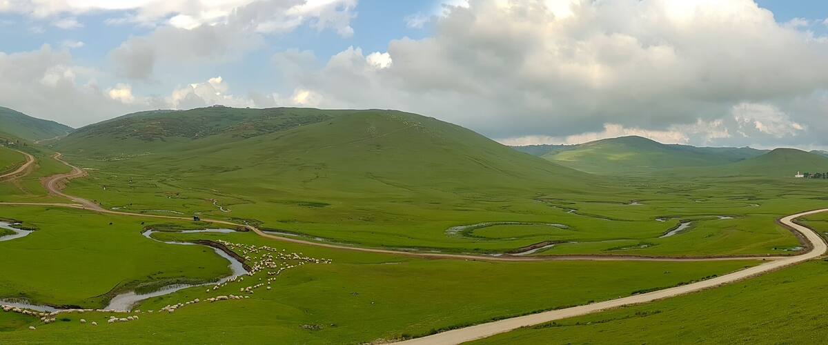 A green valley with winding roads and a river.