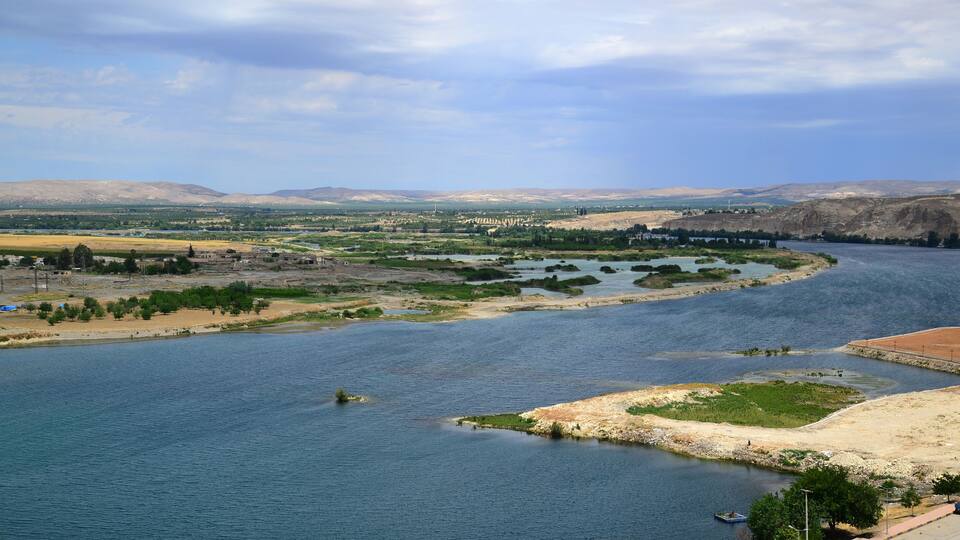 A river winding through a valley with distant mountains, a bridge, and sparse vegetation.