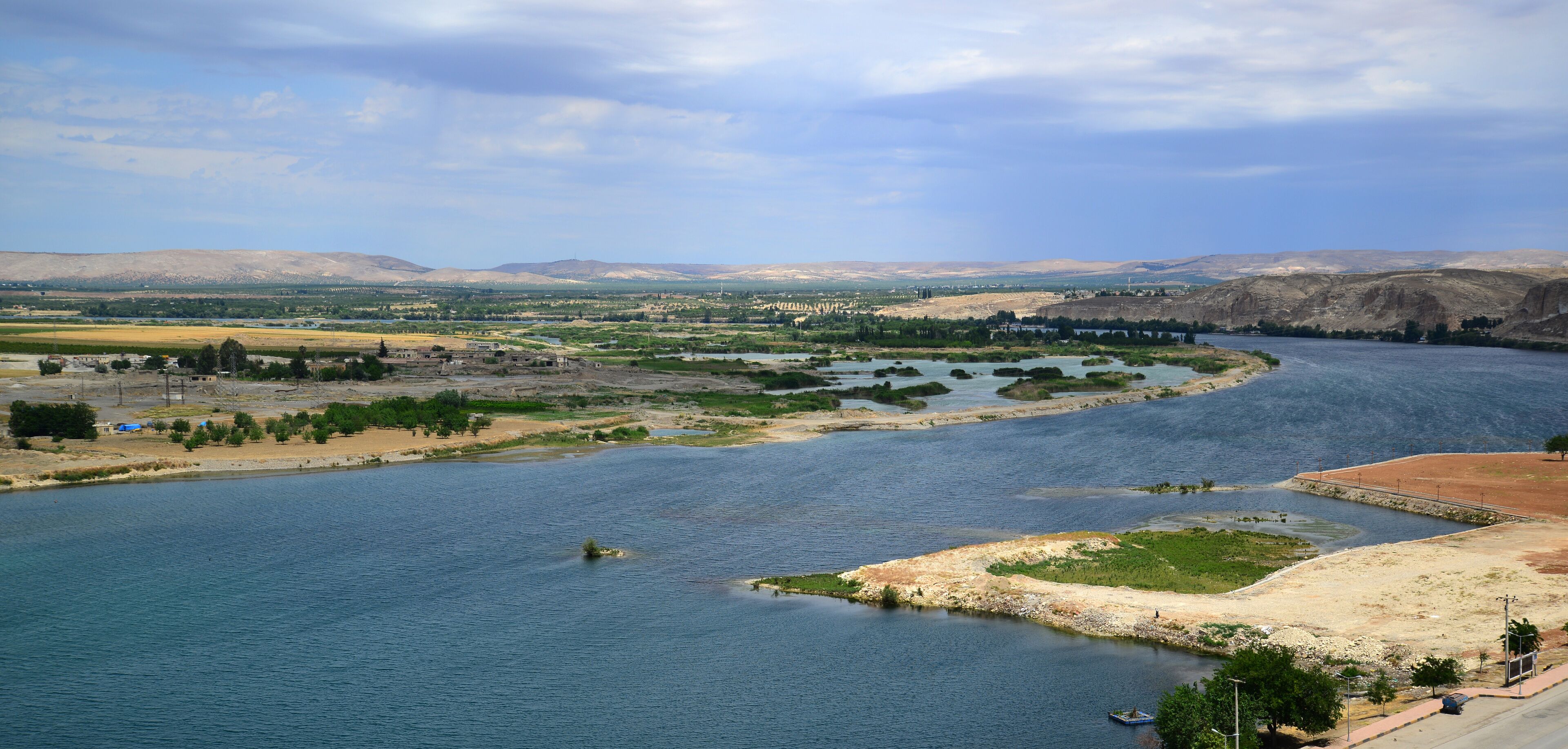 A river winding through a valley with distant mountains, a bridge, and sparse vegetation.