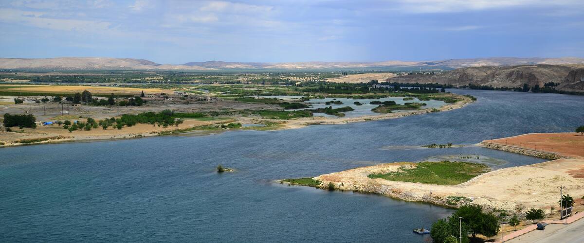 A river winding through a valley with distant mountains, a bridge, and sparse vegetation.