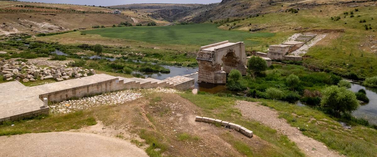 A river flowing through a valley with a stone bridge and a stone structure.