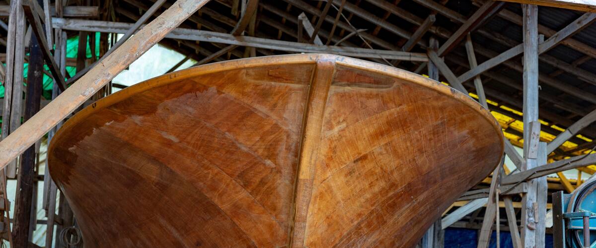 A large wooden boat under construction in a workshop with scaffolding.