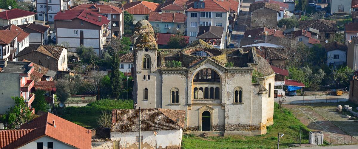A historic church with a dome and bell tower amidst a residential area with red-tiled roofs.
