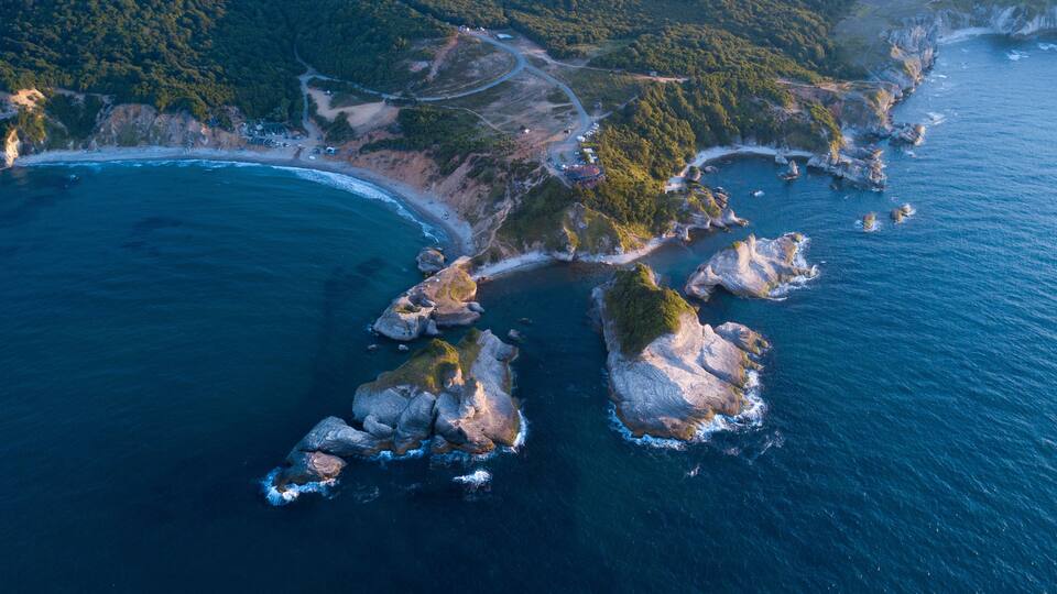 An aerial view of a coastal area with rocky outcrops, a winding road, and a beach.