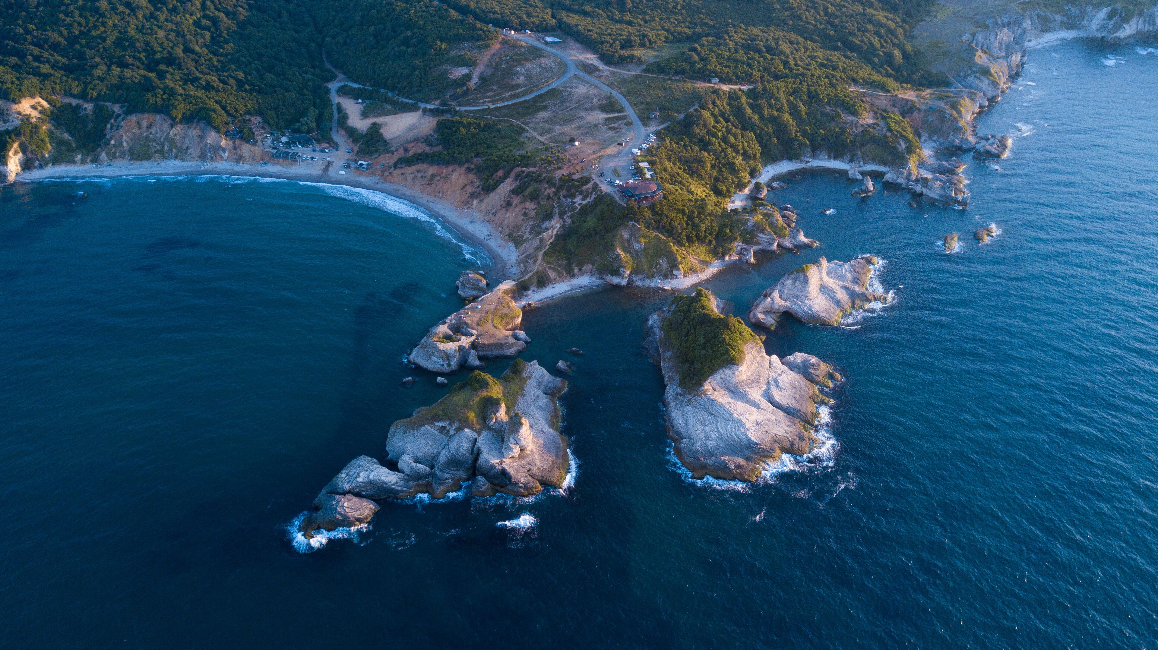 An aerial view of a coastal area with rocky outcrops, a winding road, and a beach.