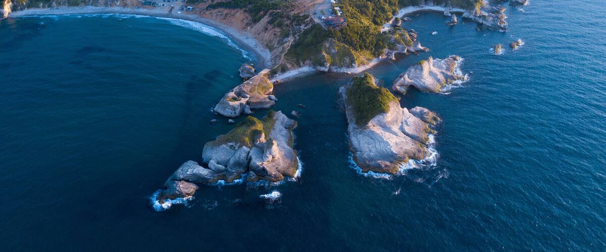 An aerial view of a coastal area with rocky outcrops, a winding road, and a beach.