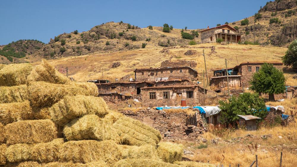 Un village rural avec des bâtiments en pierre, des bottes de foin et une colline.