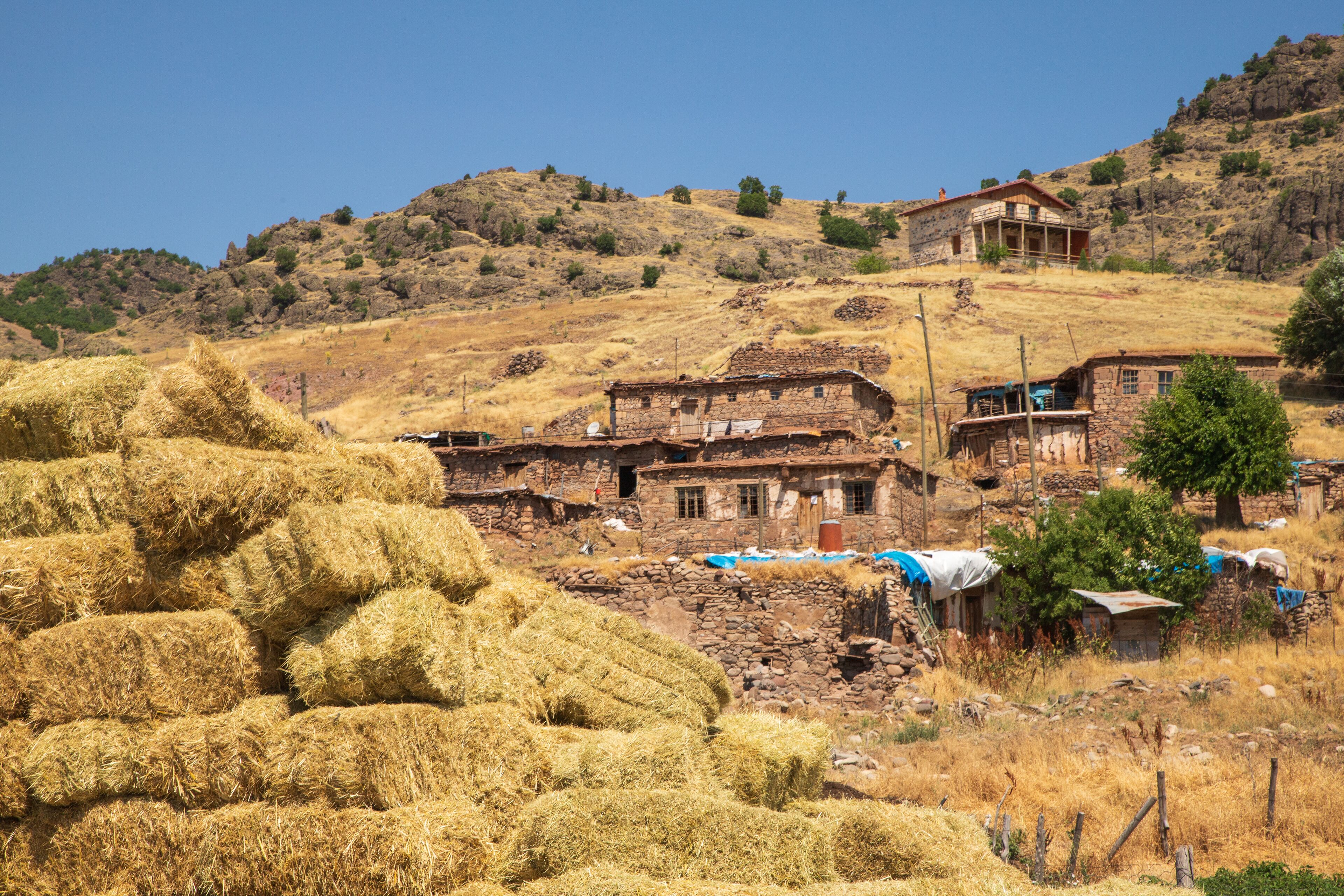 A rural village with stone buildings, hay bales, and a hillside.