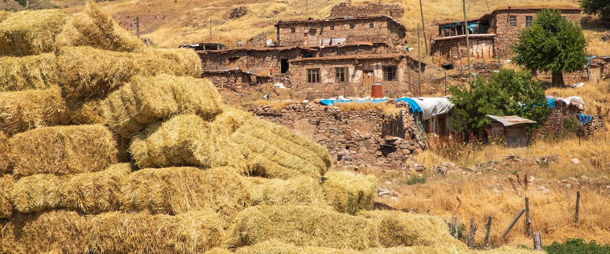 A rural village with stone buildings, hay bales, and a hillside.