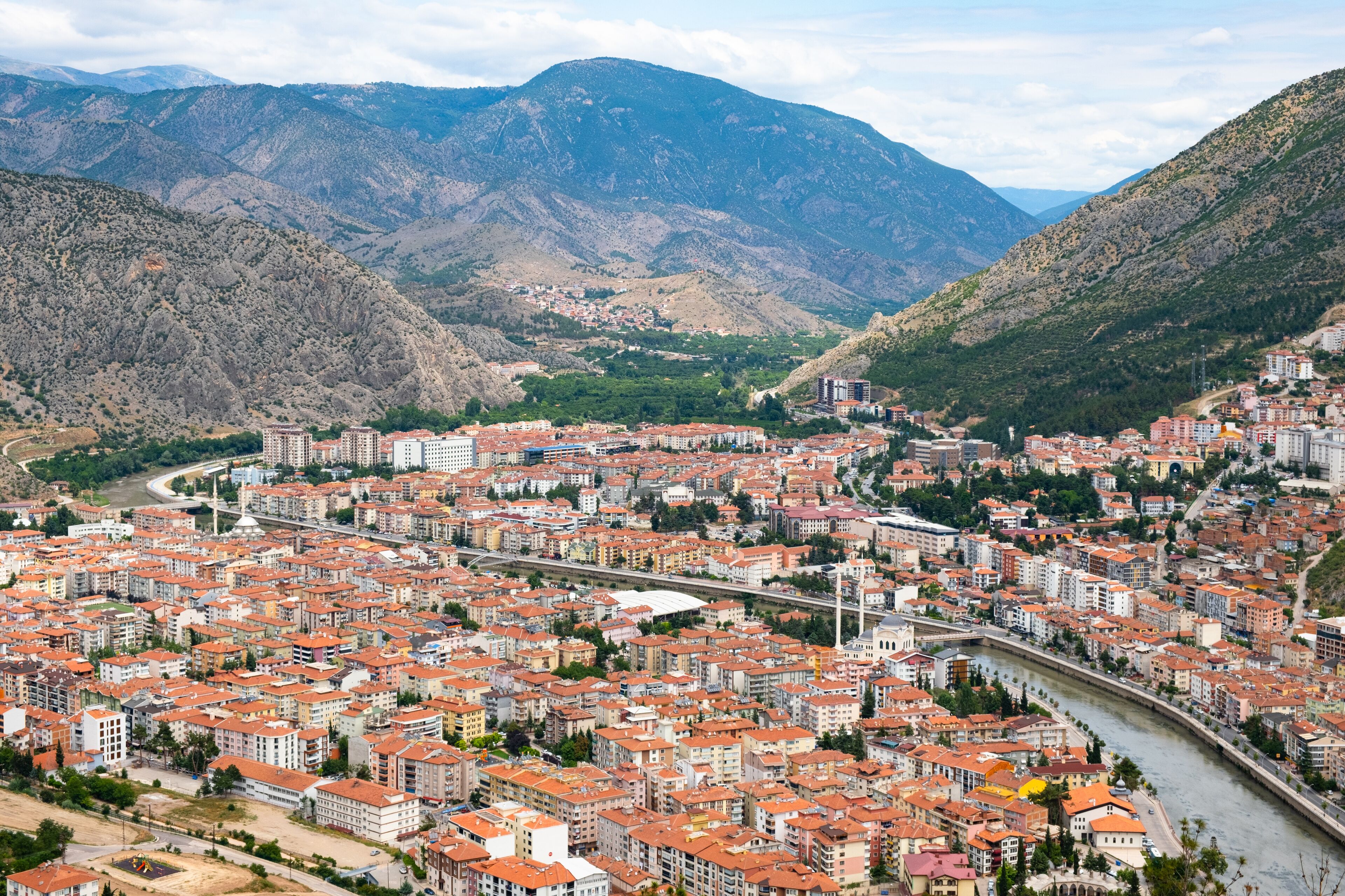 A city with red-roofed buildings nestled between mountains.