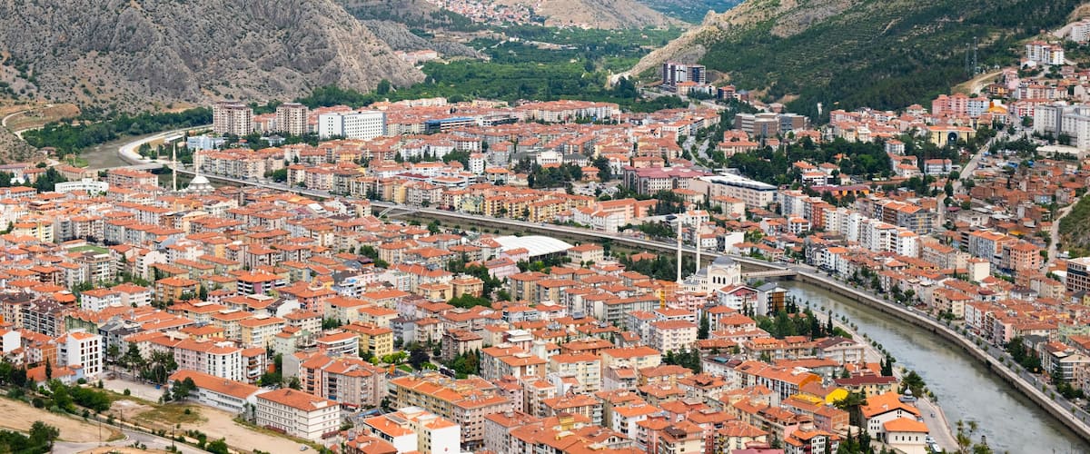 A city with red-roofed buildings nestled between mountains.