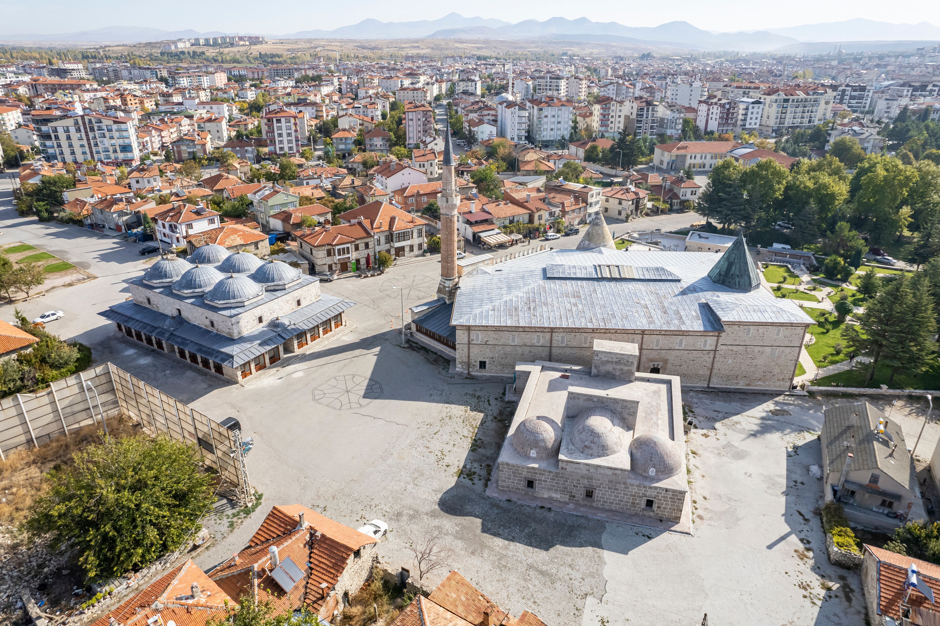 A large mosque with multiple domes and a tall minaret, surrounded by a cityscape with red-roofed buildings.