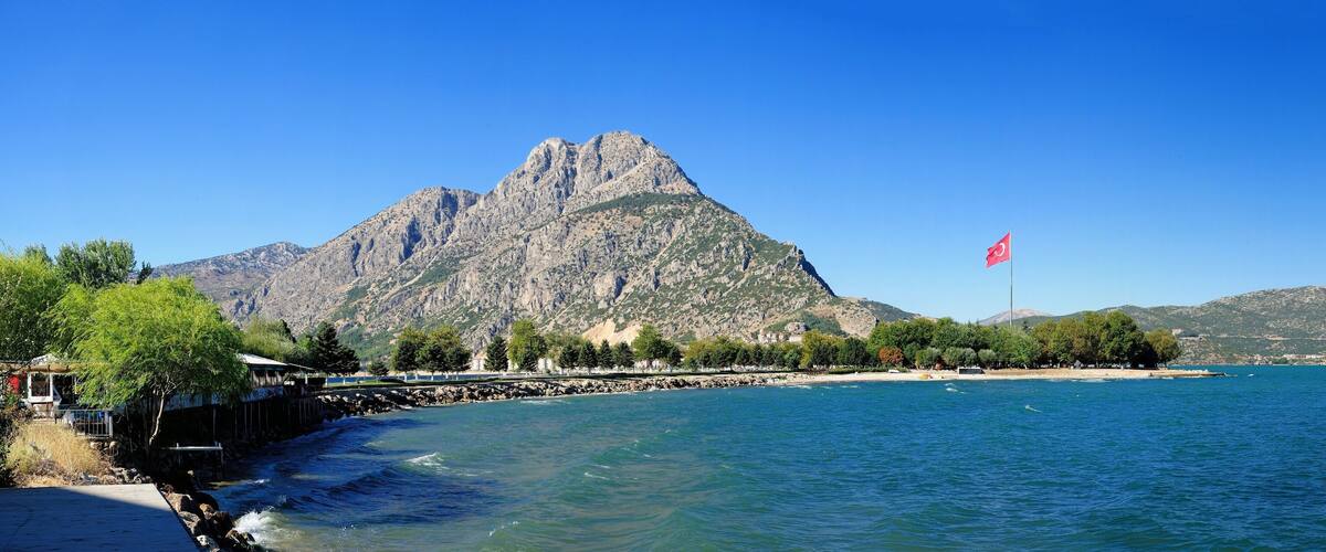 A coastal landscape with a prominent mountain, a flag on a pole, and a calm sea.