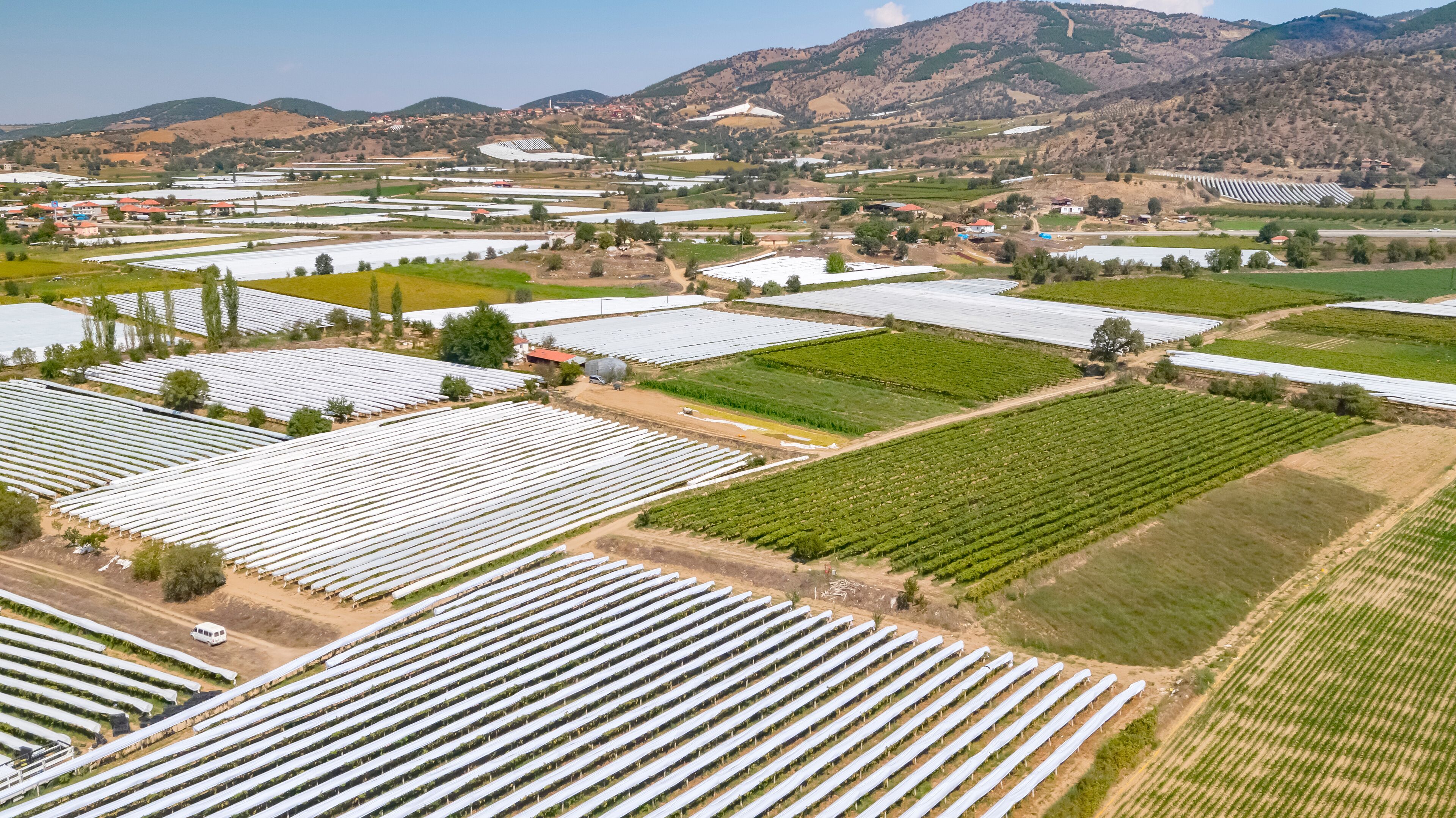 An aerial view of a large agricultural area with rows of crops and fields, surrounded by hills and a few buildings.