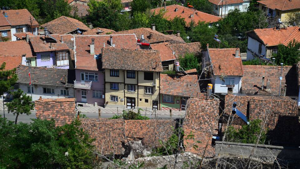 A densely packed residential area with terracotta-tiled roofs, surrounded by greenery and trees.