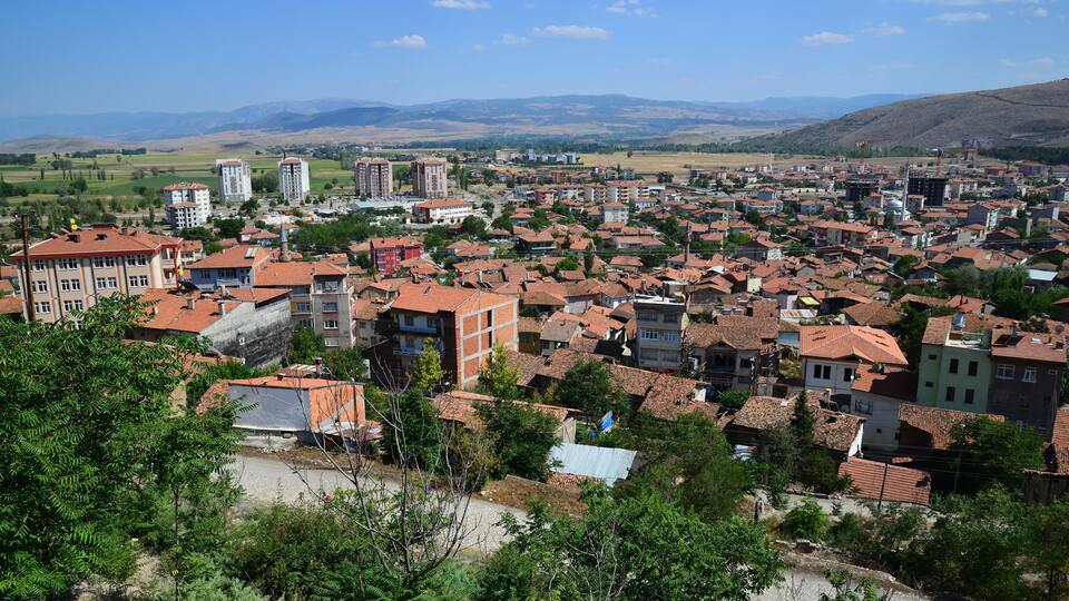 A town with red-tiled roofs, surrounded by green hills and mountains.