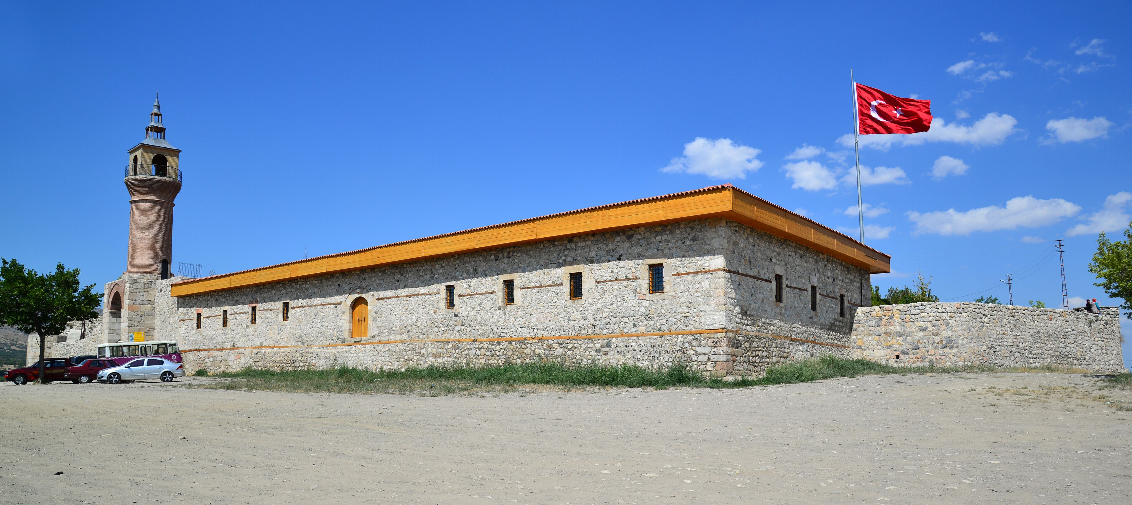 A stone building with a red flag, a tower, and parked cars.