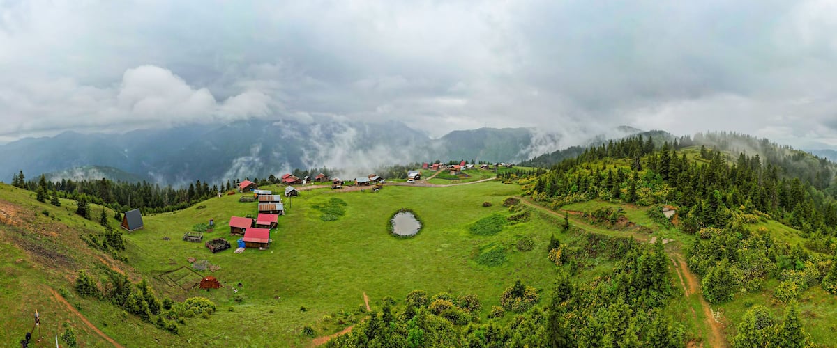 A mountainous landscape with a small village, green fields, and a pond.