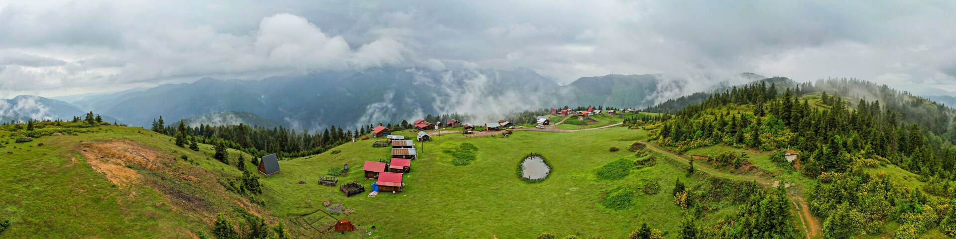 A mountainous landscape with a small village, green fields, and a pond.