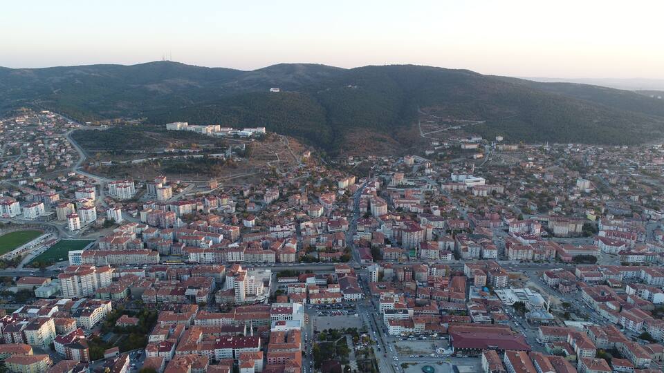 A cityscape with dense residential buildings, a central square, and surrounding hills.