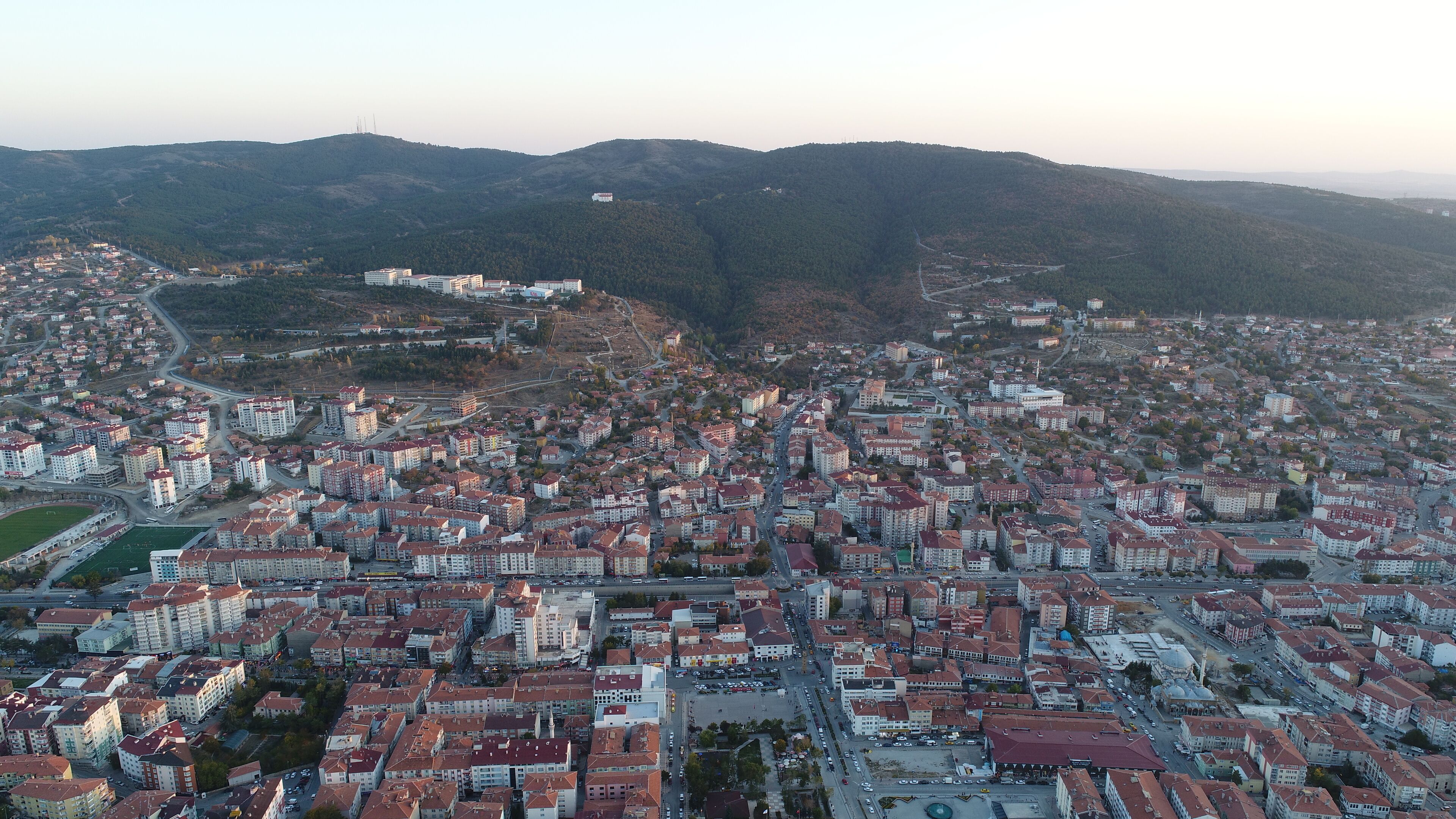 A cityscape with dense residential buildings, a central square, and surrounding hills.