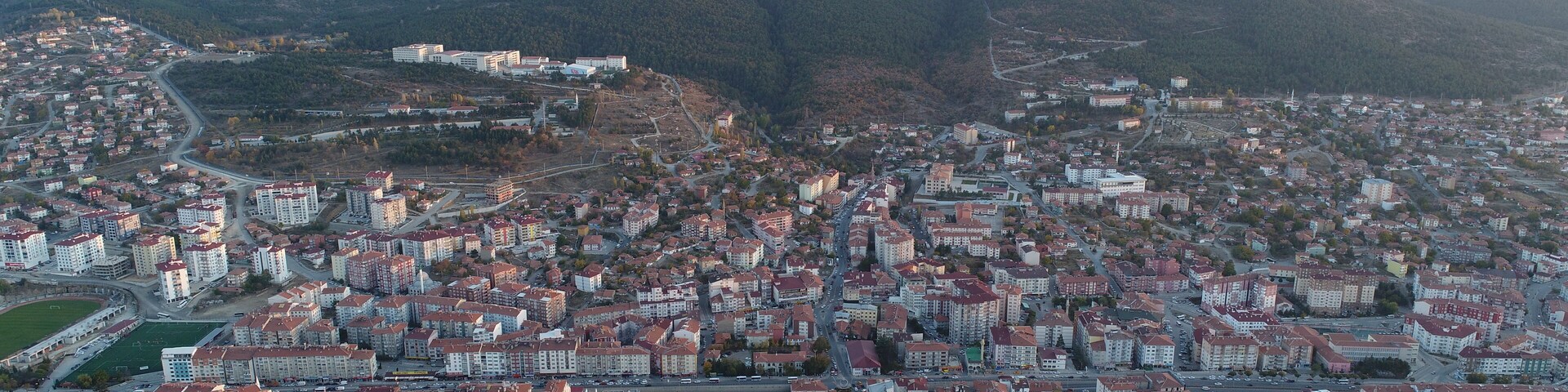 A cityscape with dense residential buildings, a central square, and surrounding hills.