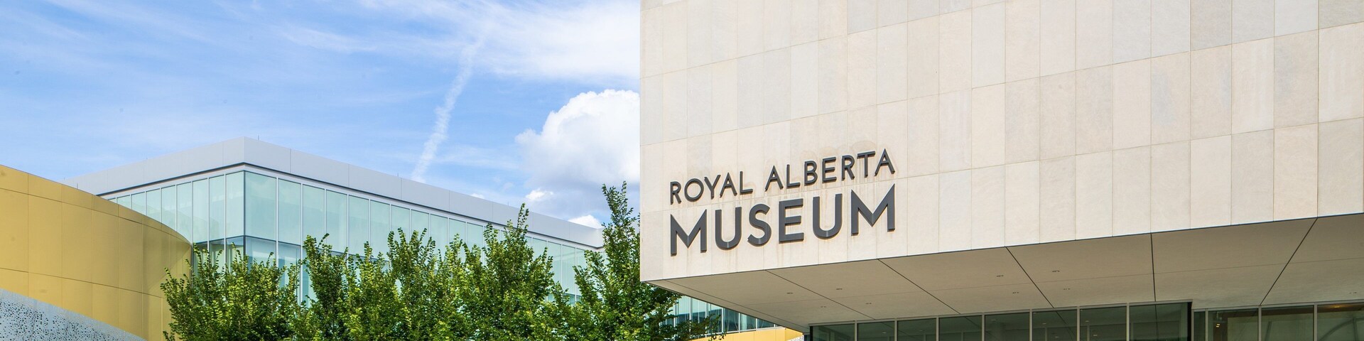 Entrada del Museo Real de Alberta, con puertas de vidrio y un cielo azul claro.