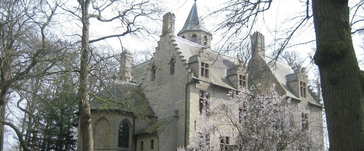 A historic building with a prominent tower, surrounded by trees and blooming flowers.