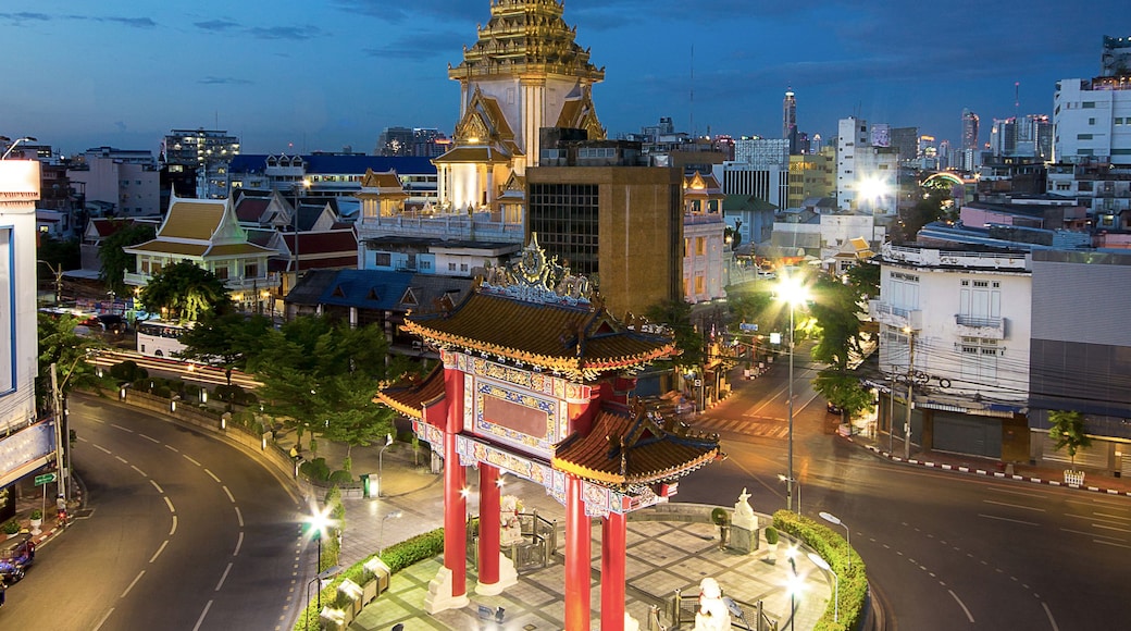 A cityscape at dusk with a prominent temple featuring a tall spire and a traditional pavilion with red pillars.