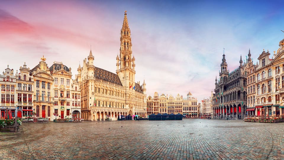 A historic European square with ornate buildings, a prominent tower, and cobblestone pavement.