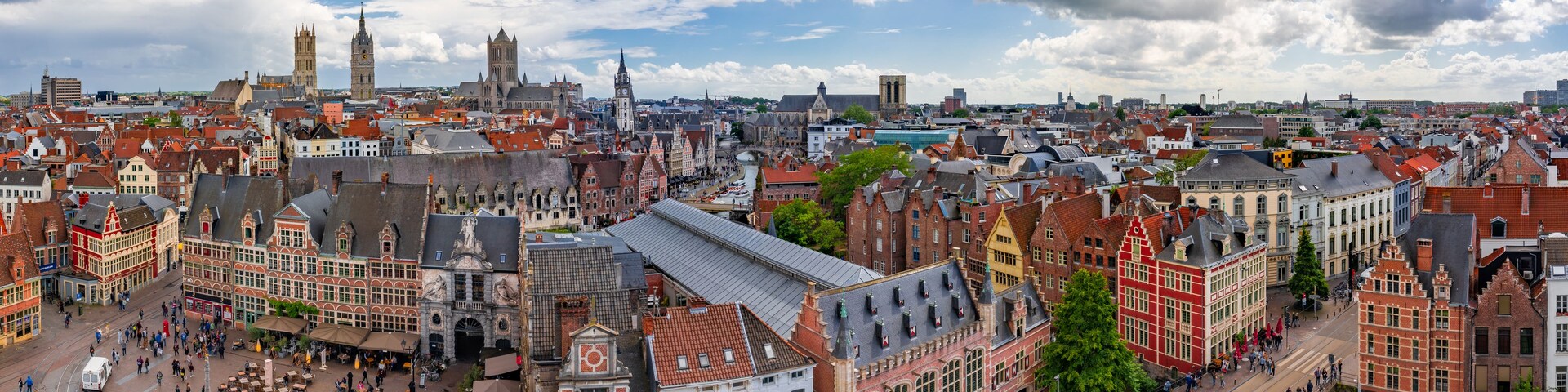 Paisagem urbana densa com edifícios históricos, uma torre do relógio imponente e um rio cortando o centro.
